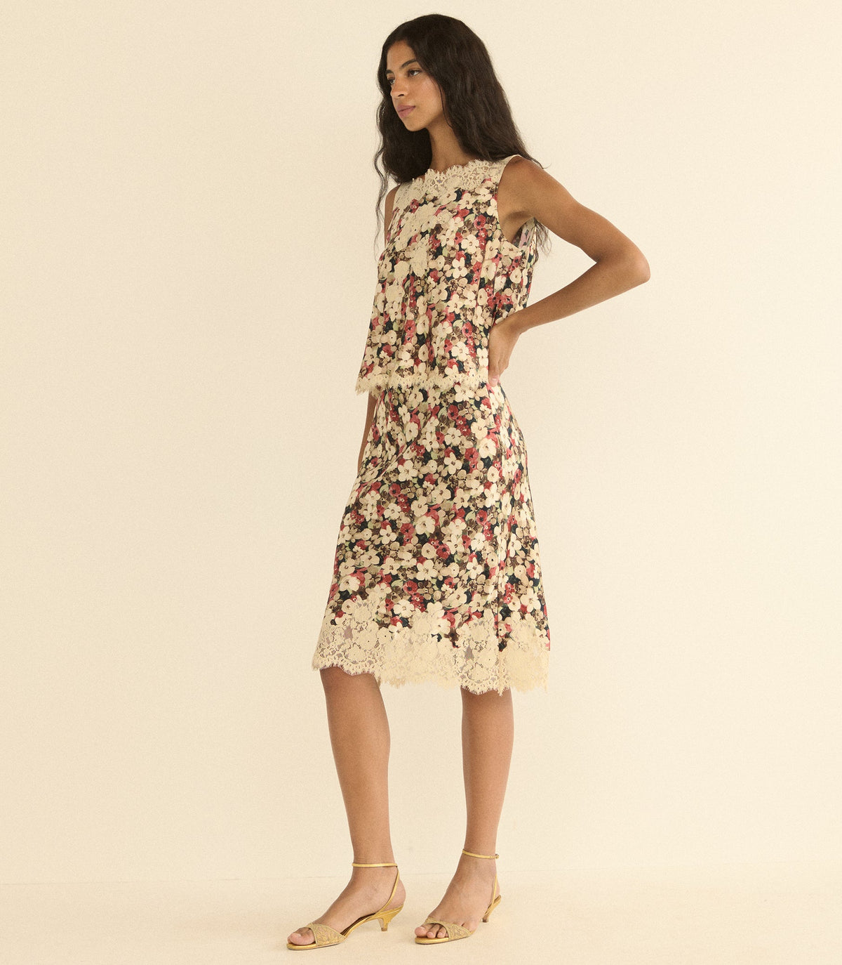 A woman models a matching set featuring a sleeveless top with a dense floral print in cream, pink, and green, finished with a cream lace hem, set against a solid cream background.
