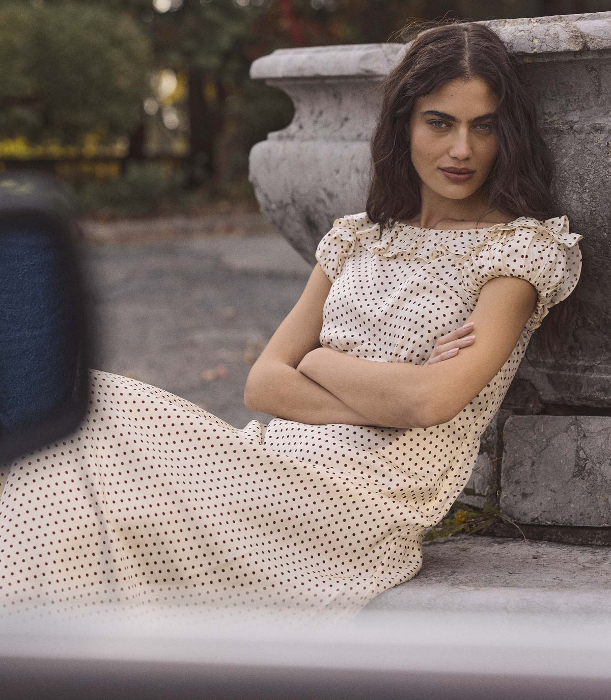 Woman in a polka dot dress sitting against a stone wall outdoors