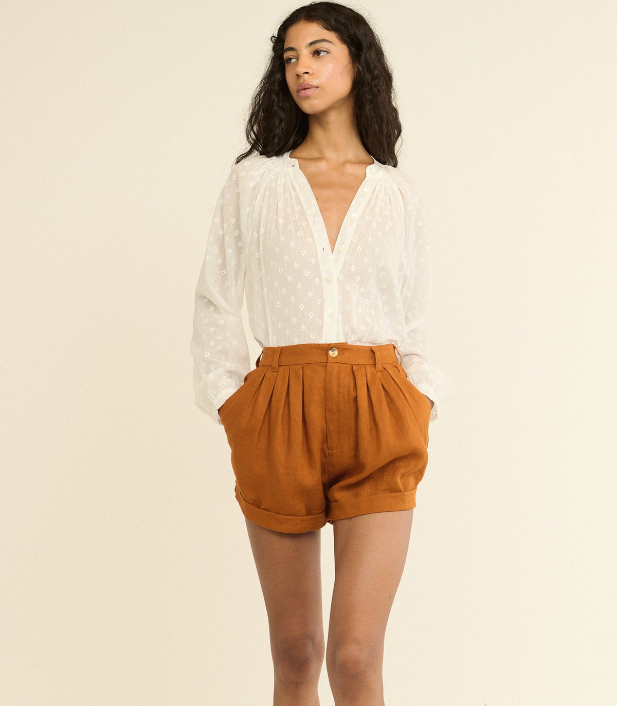 Woman wearing a white blouse and brown shorts on a beige background